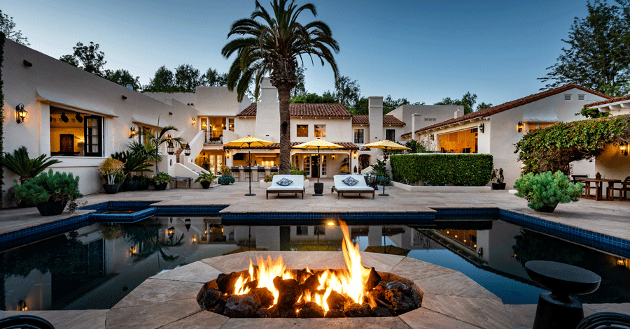 View from fire pit of pool, lounge chairs, and luxury Spanish-style home