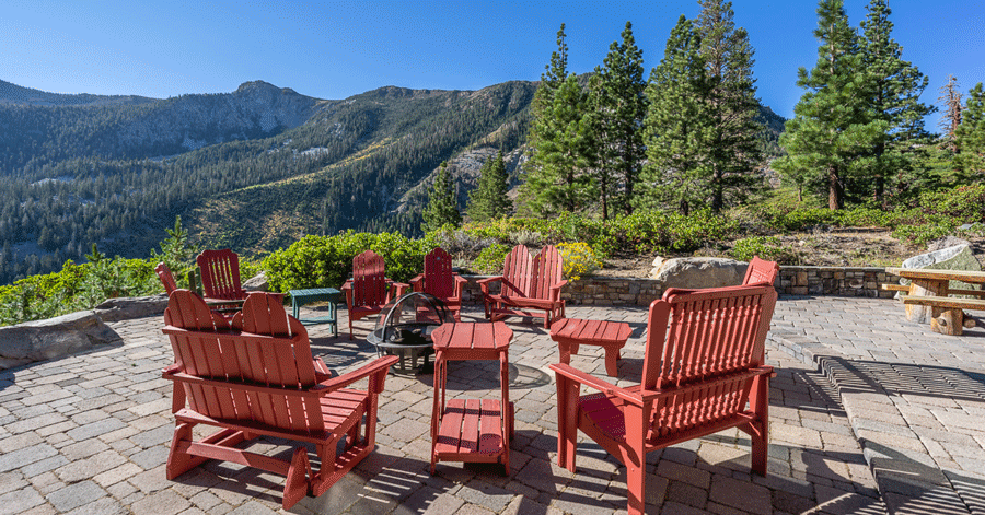Red Adirondack chairs circled around a fire pit on a brick patio in the mountains