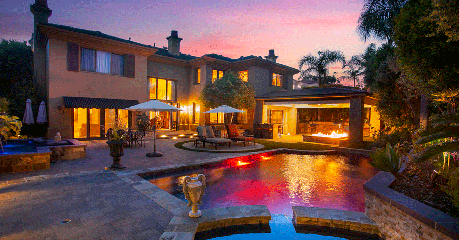 View from pool and spa of home at evening with colored lights in the pool