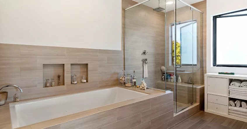 Baño principal con ducha con paredes de vidrio, bañera grande y lujosos pisos y paneles de madera marrón
